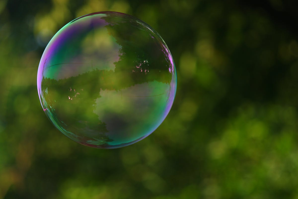 The bubble A single soap bubble floating against a soft green background, its surface swirling with iridescent color